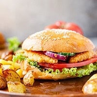 Assembled crispy chicken burger with lettuce, tomato, onion, and cucumber on a sesame bun