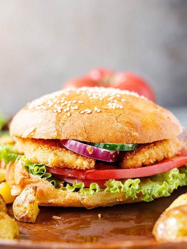Assembled crispy chicken burger with lettuce, tomato, onion, and cucumber on a sesame bun