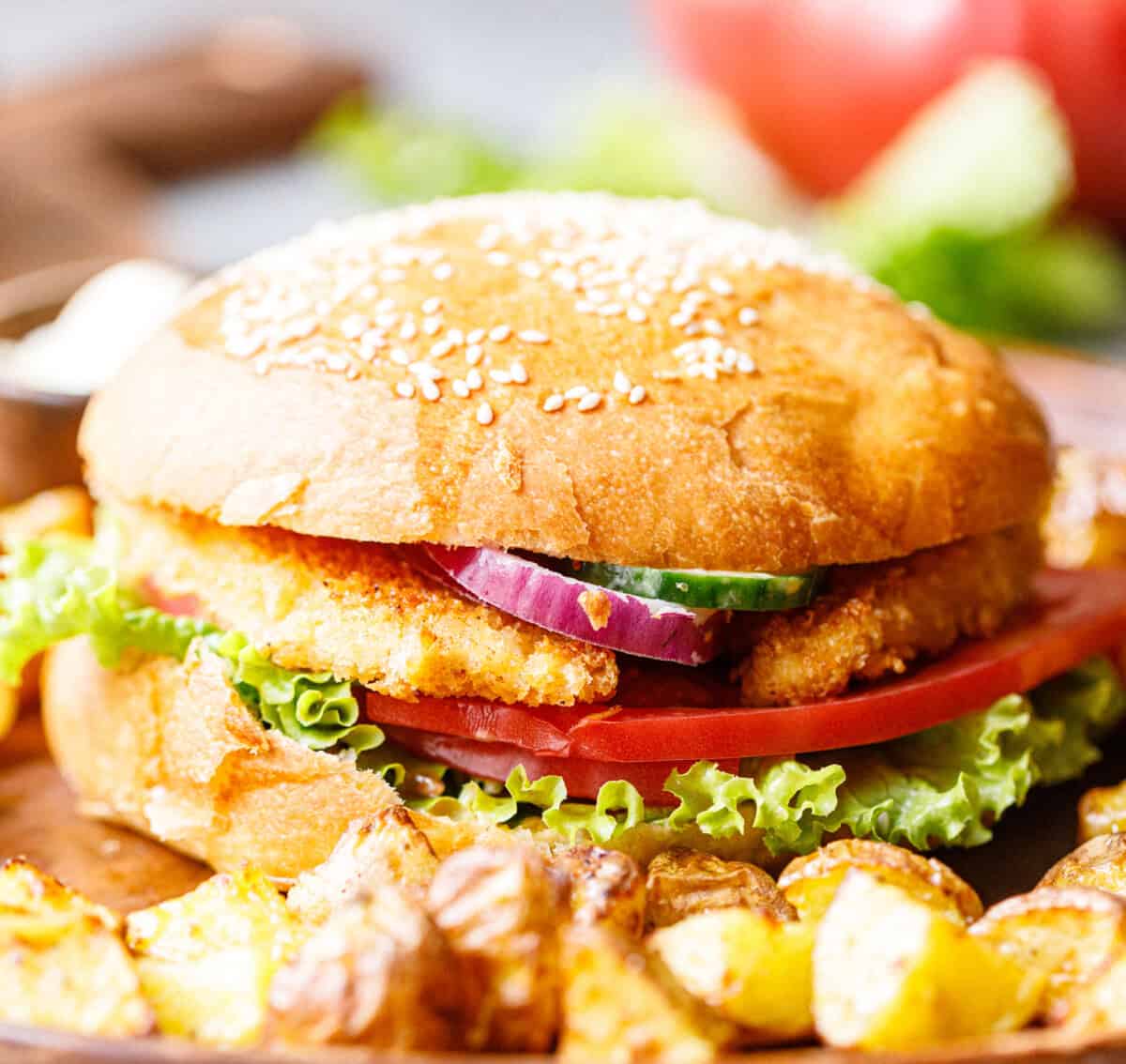 Crispy chicken burger served with roasted potatoes on a wooden plate