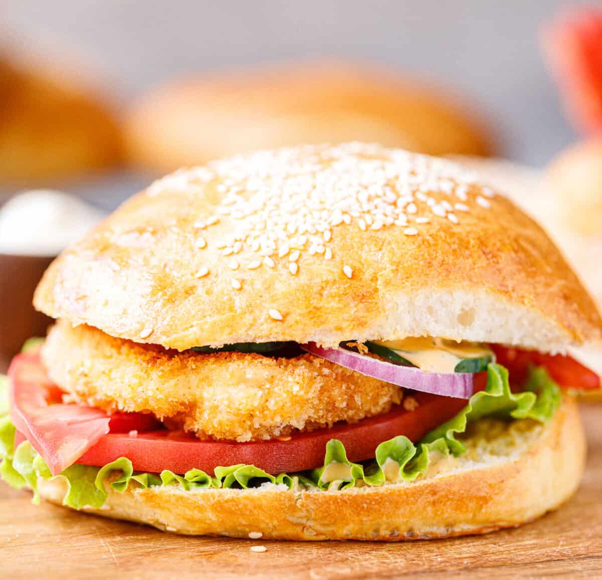 Assembled crispy chicken burger with lettuce, tomato, onion, and cucumber on a sesame bun
