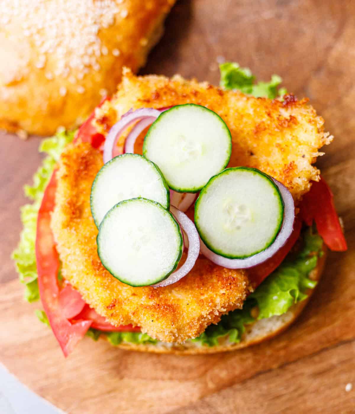 Breaded chicken burger topped with cucumber slices and red onion on a sesame bun