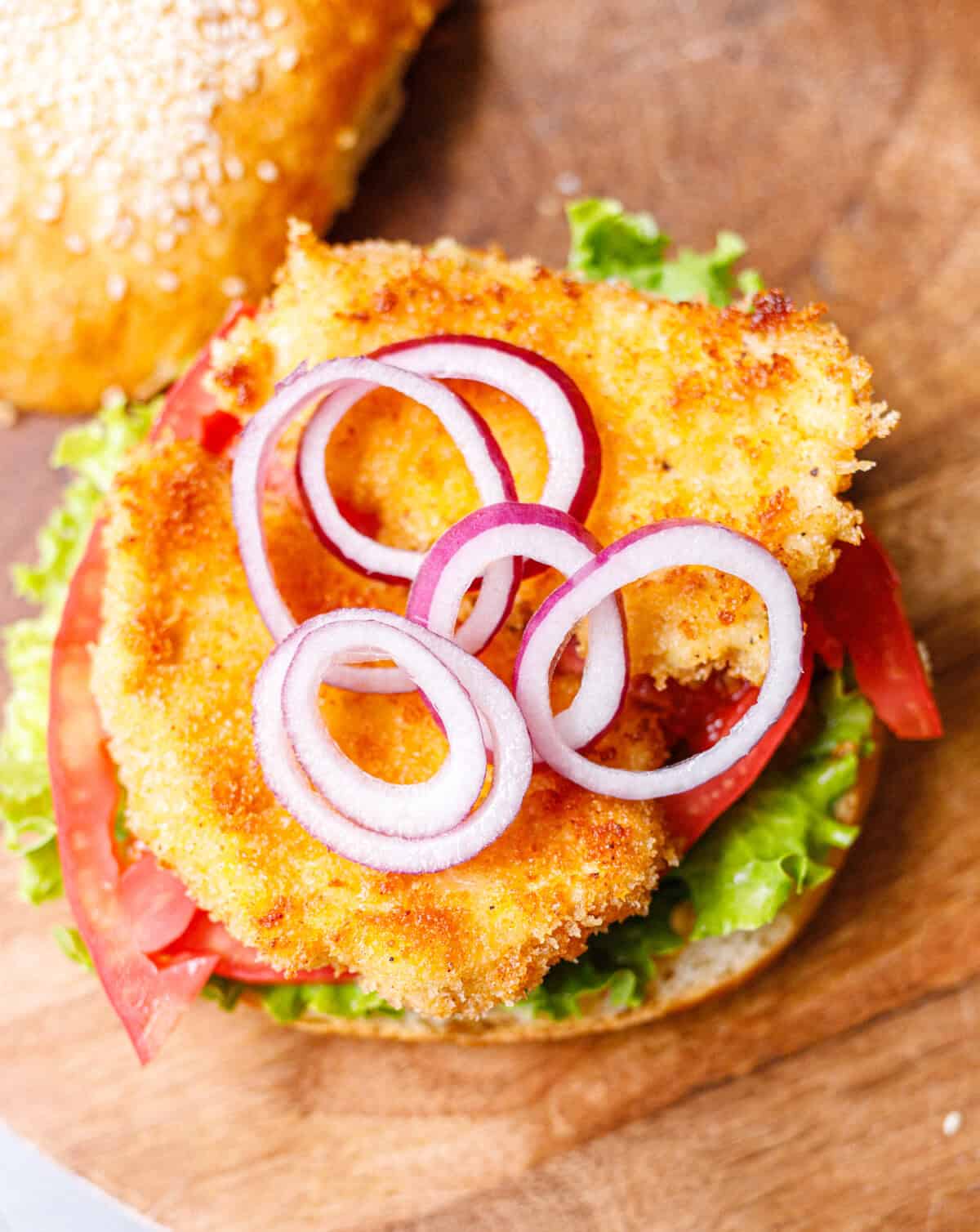 Crispy chicken burger topped with red onion rings, tomato, and lettuce on a brioche bun