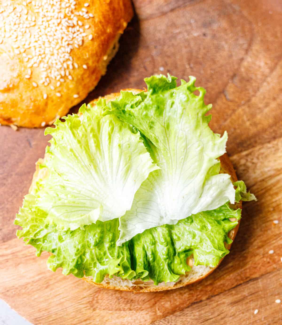 Crisp lettuce leaves on a sauced brioche bun bottom for a crispy chicken sandwich