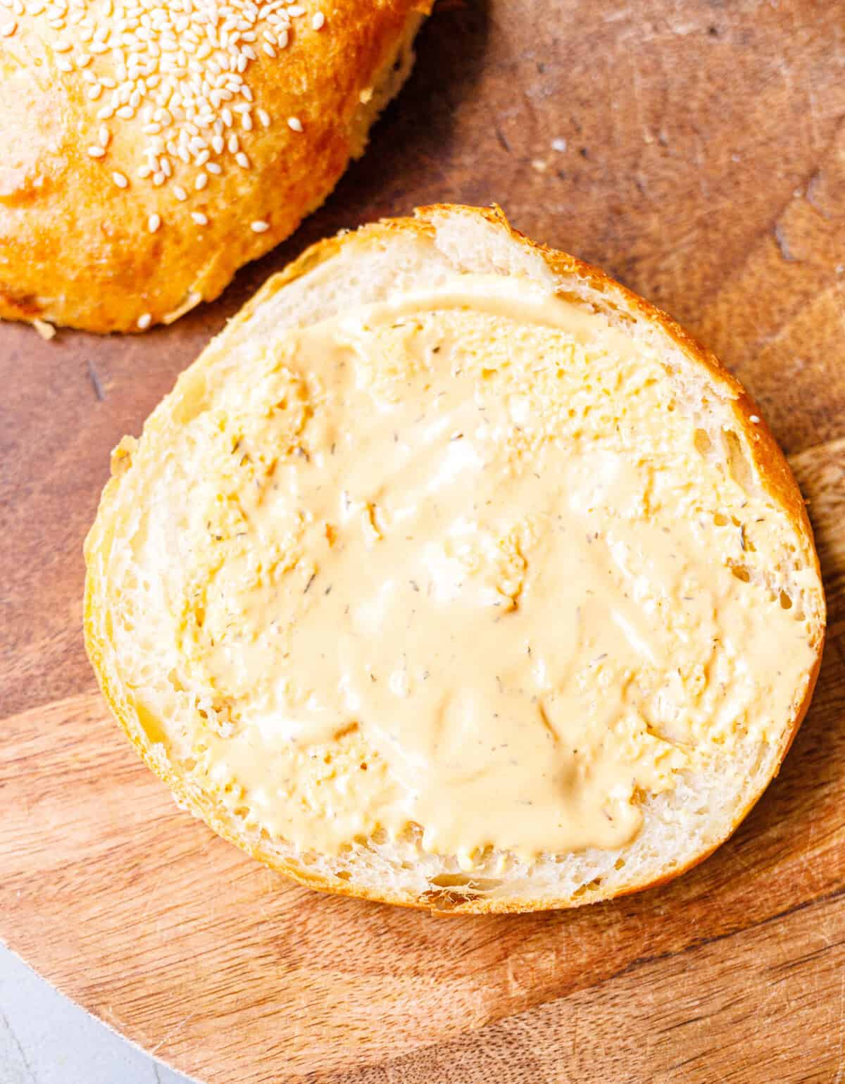 Toasted brioche burger bun half spread with herb butter on a wooden board