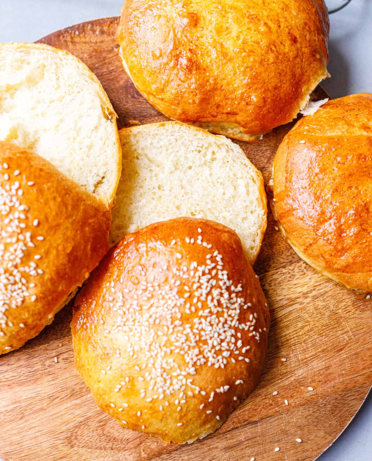Homemade brioche buns on a wooden board, some sliced to show the soft crumb