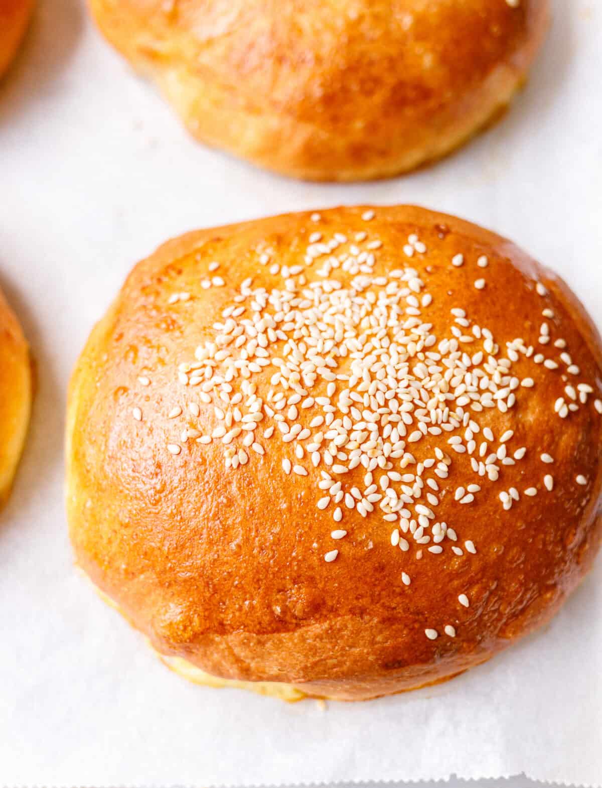 Golden brioche burger bun topped with sesame seeds on parchment paper
