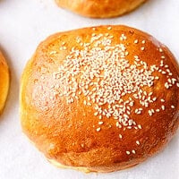 Golden brioche burger bun topped with sesame seeds on parchment paper
