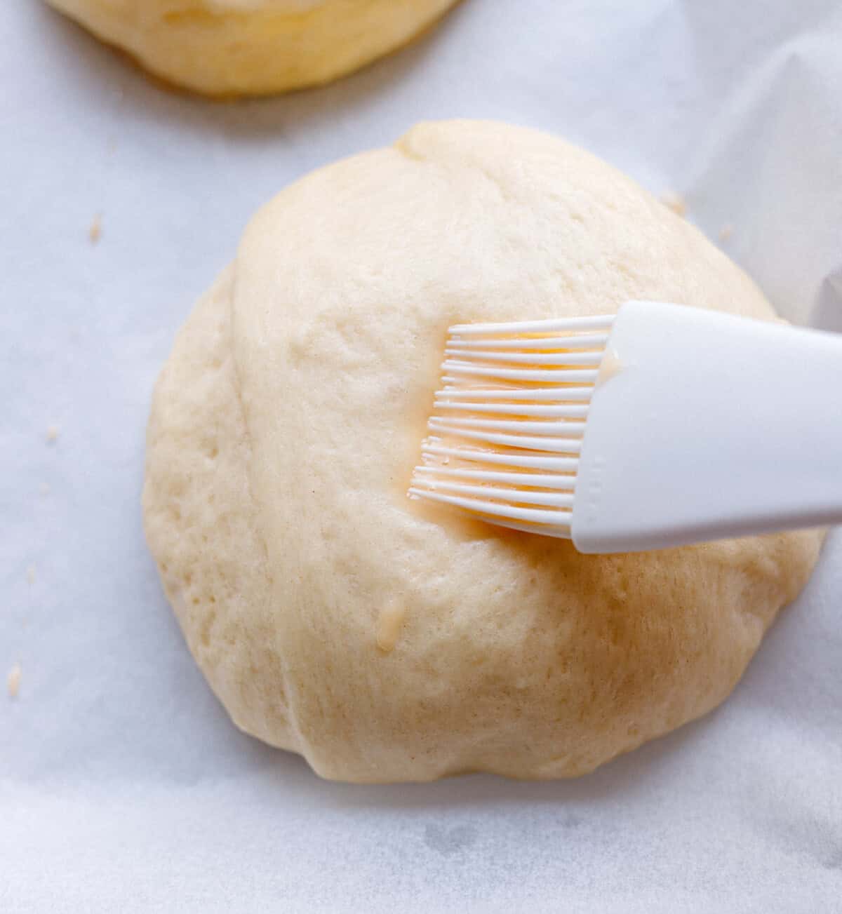 Two proofed brioche burger bun dough balls on parchment paper