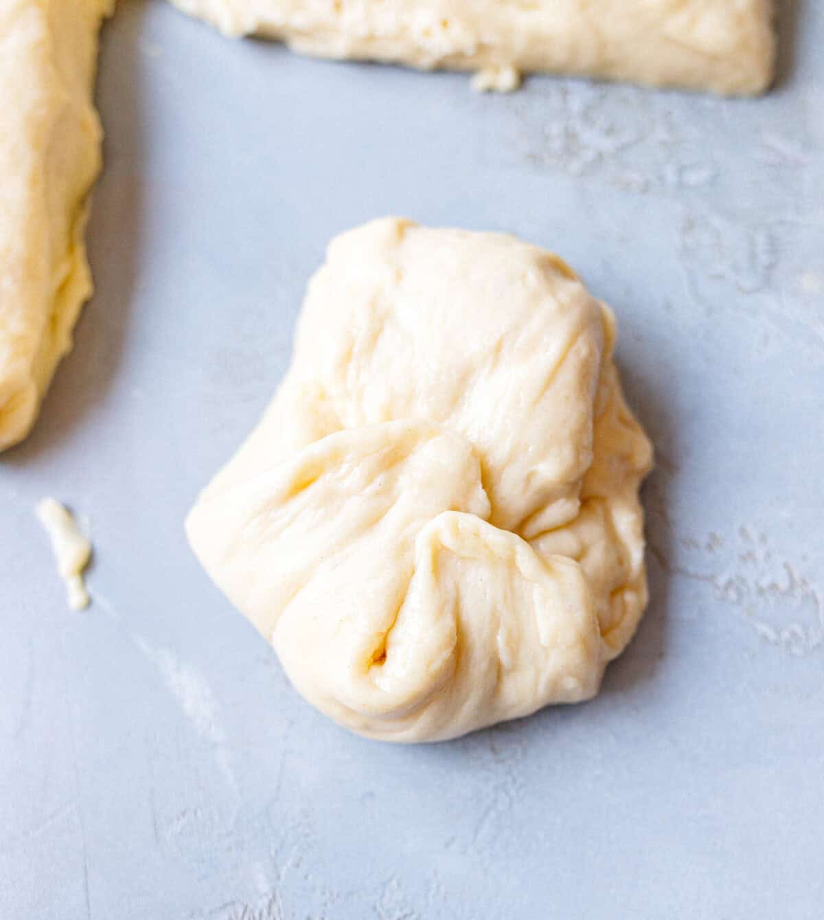 Hand-shaped brioche dough with the seam pinched closed underneath