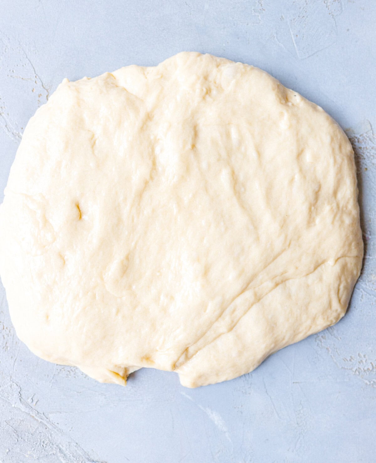 Risen brioche dough pressed into a flat round on a floured surface