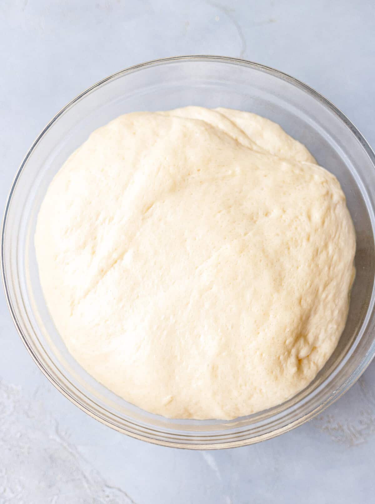 Brioche burger bun dough doubled in size in a glass bowl after the first rise