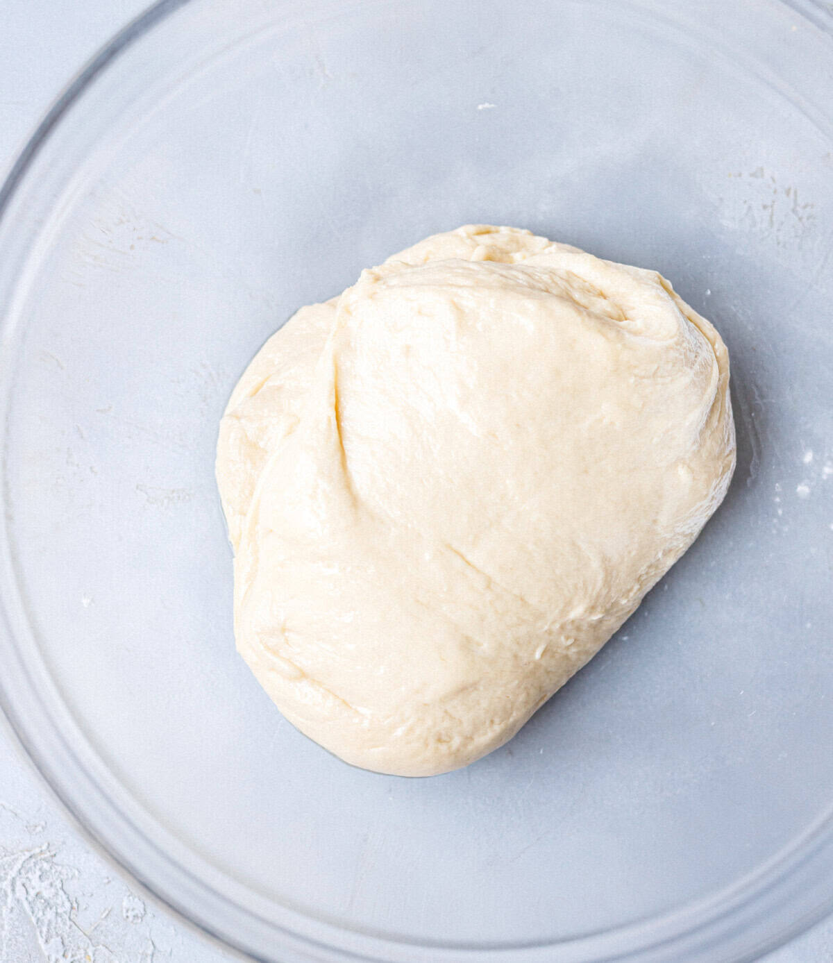 Smooth ball of brioche dough resting in a greased glass bowl before rising