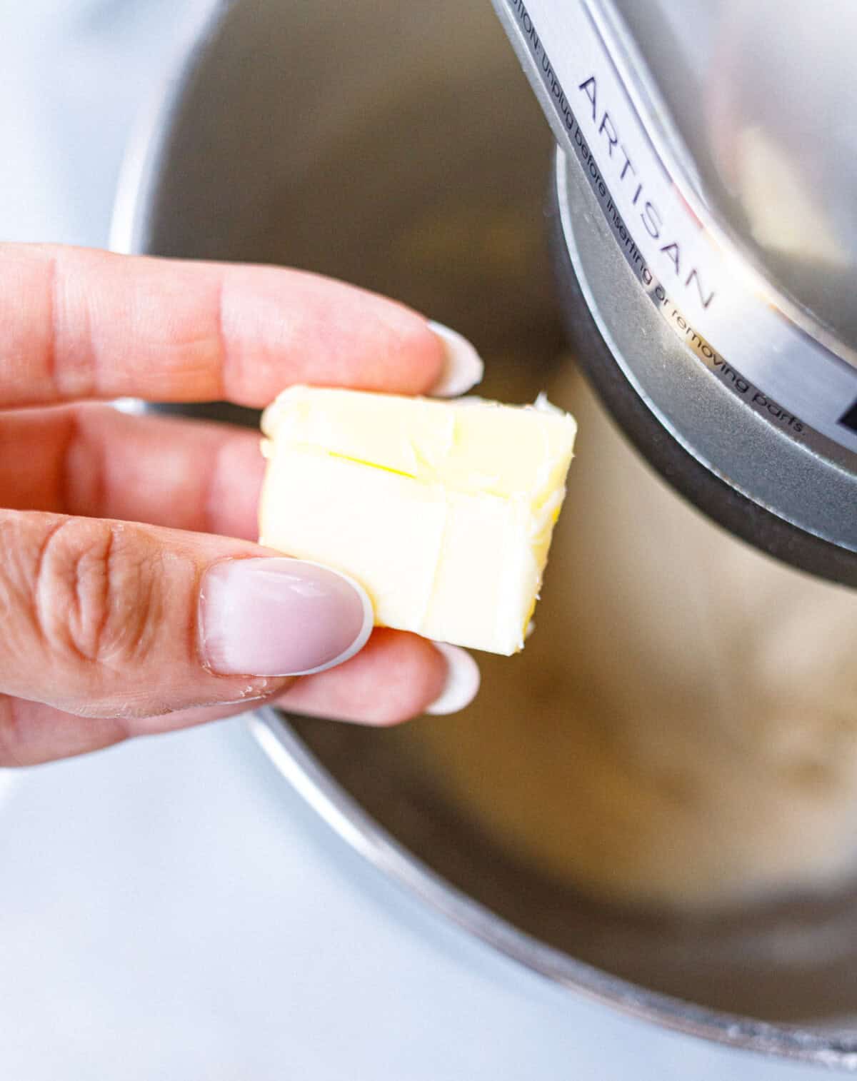 Adding a piece of softened butter to brioche dough in a stand mixer bowl