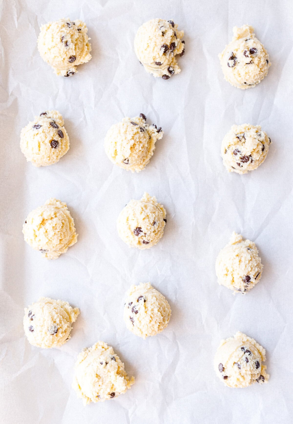Scooped balls of cottage cheese cookie dough on a parchment lined baking sheet