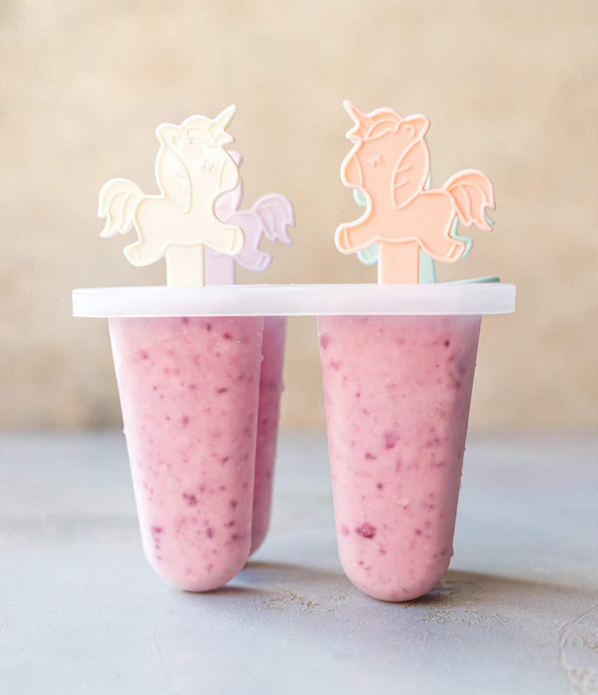 Two pink cottage cheese popsicles in a mold with unicorn sticks, before dipping in chocolate