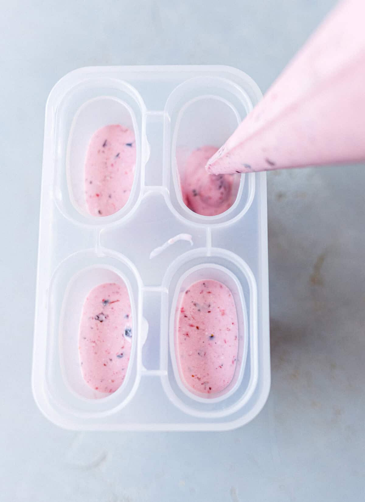 Piping pink cottage cheese and berry mixture into a four-cavity popsicle mold
