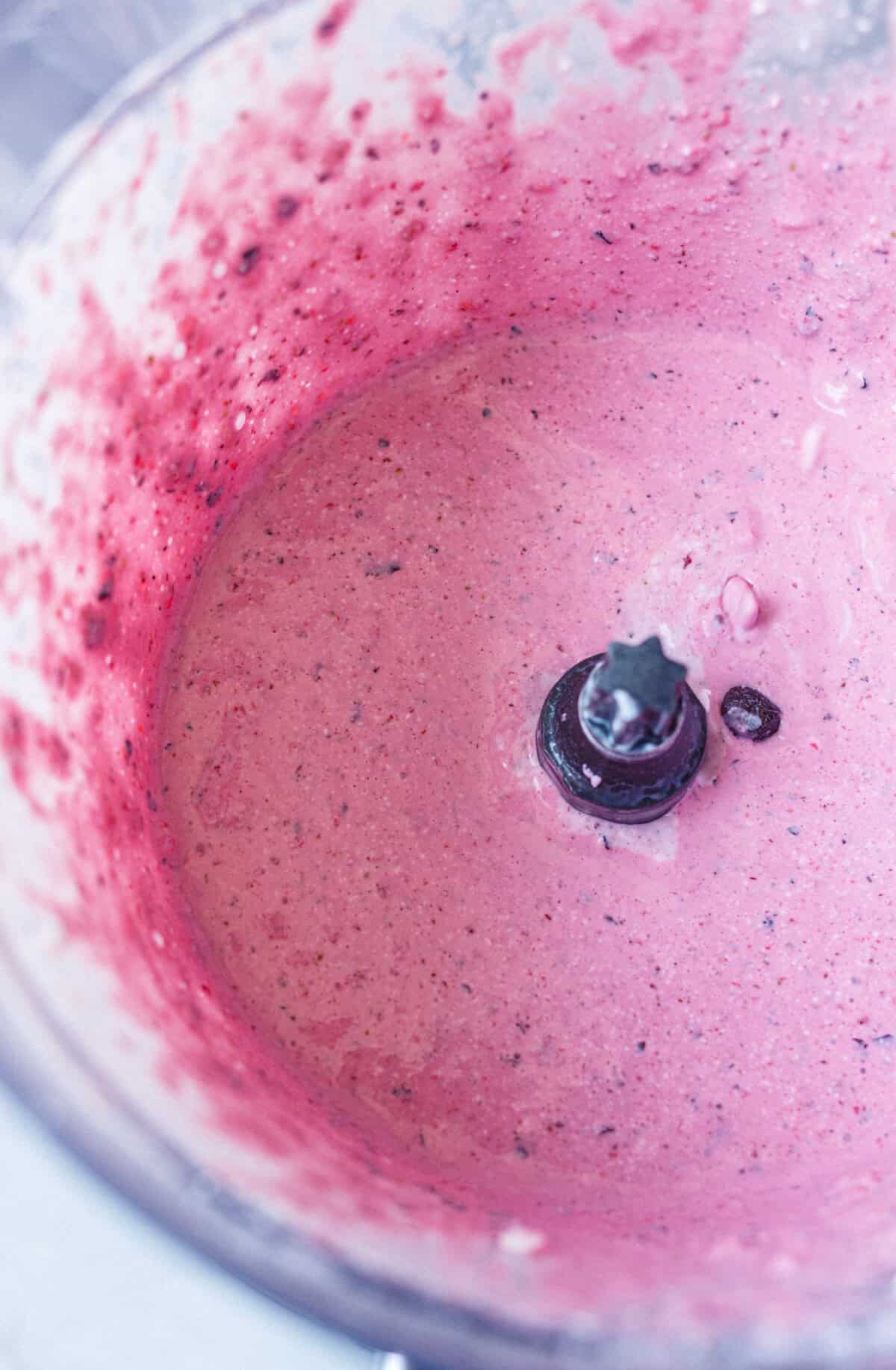 Blended cottage cheese and mixed berry mixture in a food processor, smooth and pink