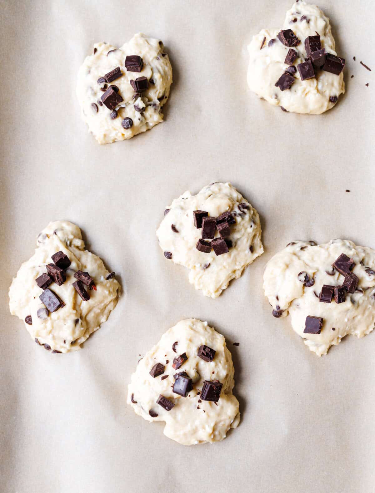 6 scoops of cottage cheese scone dough on parchment topped with chunks of dark chocolate