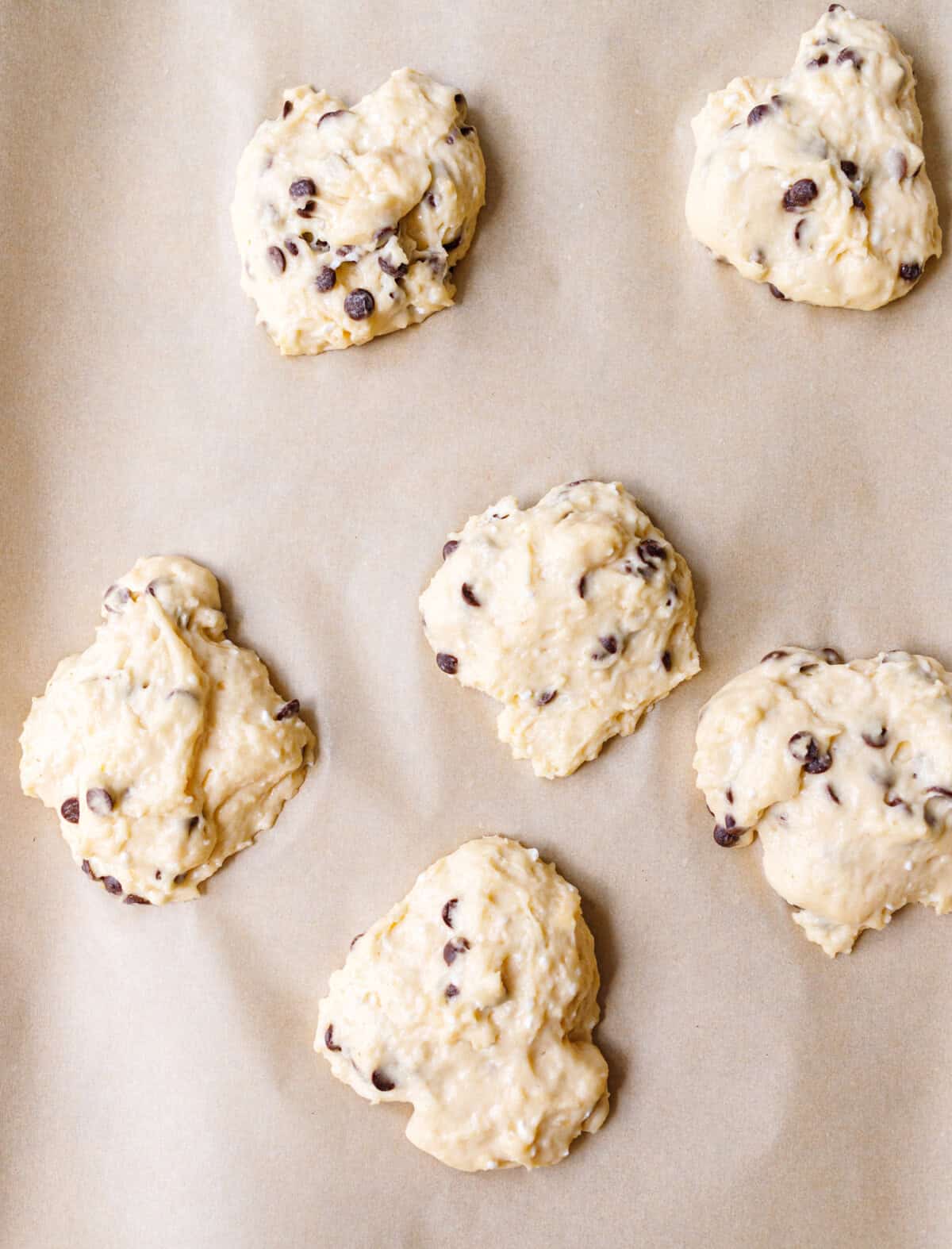 Five mounds of chocolate chip scone dough spaced apart on a parchment lined baking sheet