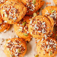 Red lentil bread rolls topped with sesame, flax, and pumpkin seeds, stacked on parchment paper