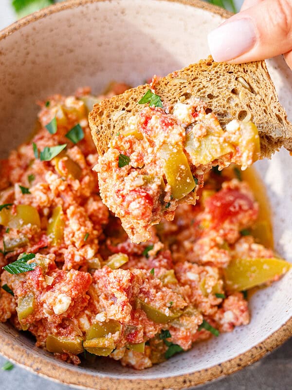 Hand dipping a piece of toasted bread into a bowl of Bulgarian mish mash