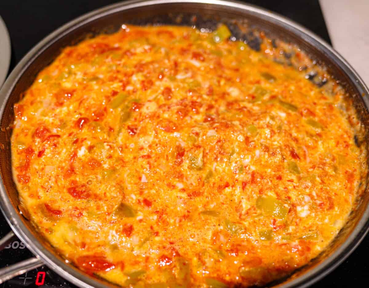 Beaten eggs poured over cooked peppers and tomatoes in a skillet before setting