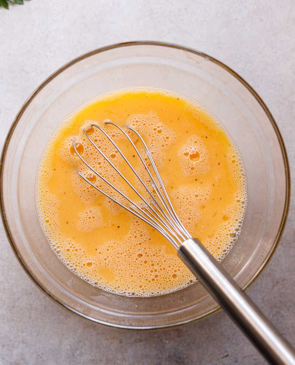 Six beaten eggs in a glass bowl with a whisk