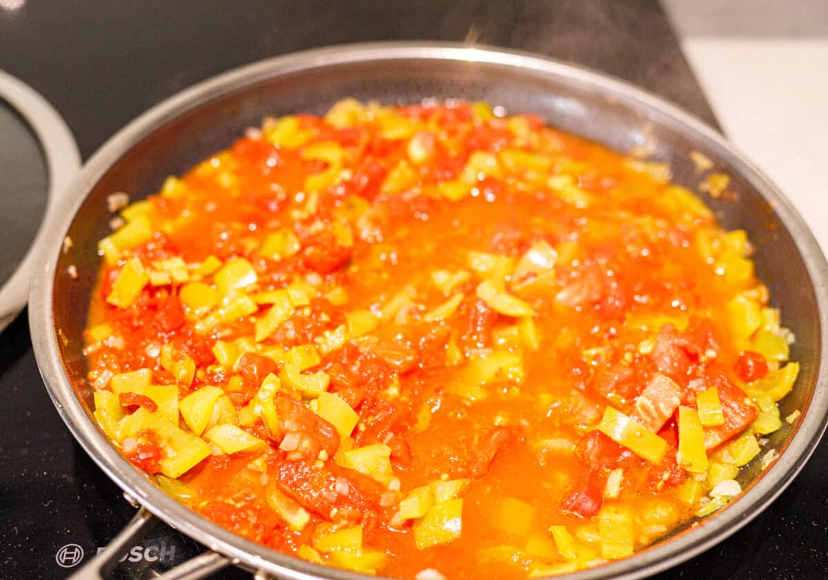 omatoes and peppers simmering down in a skillet with visible liquid