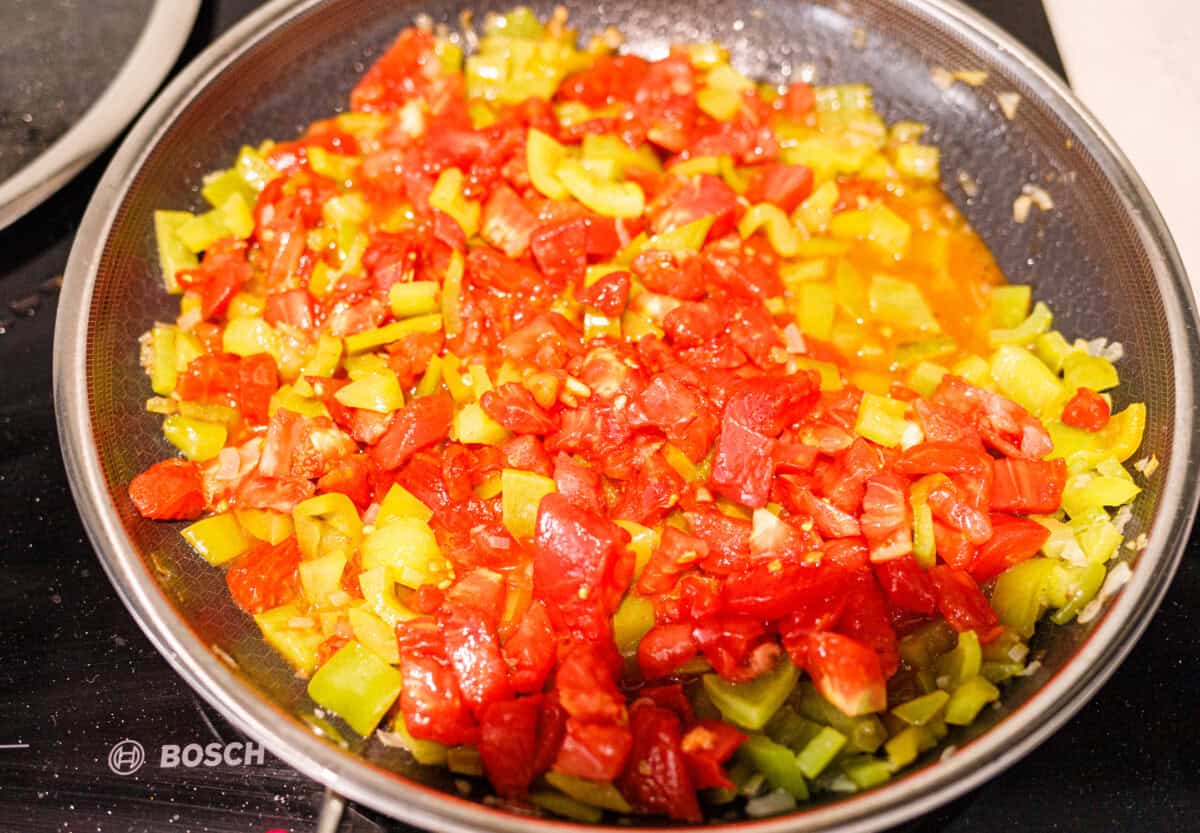Chopped tomatoes added to the cooked peppers and onion in a skillet