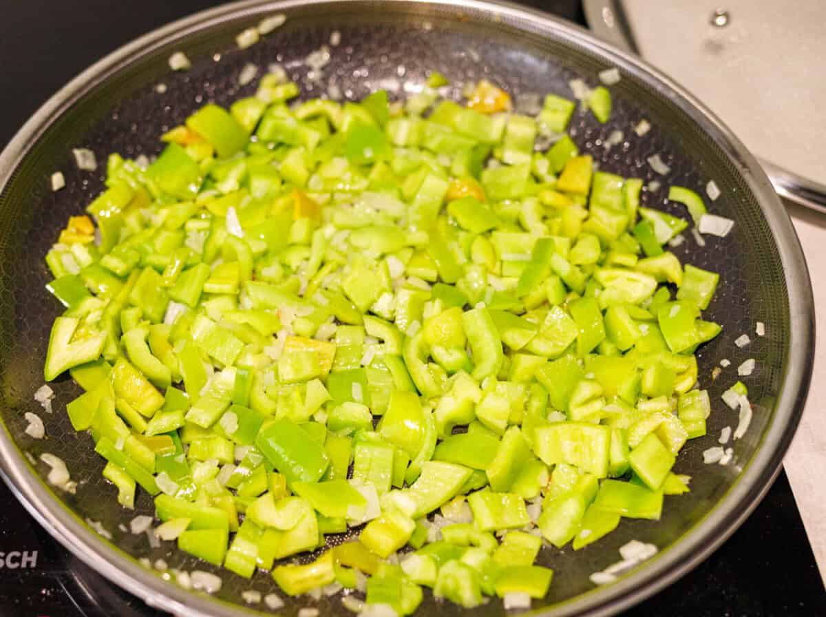 Chopped green peppers added to the softened onion in a skillet