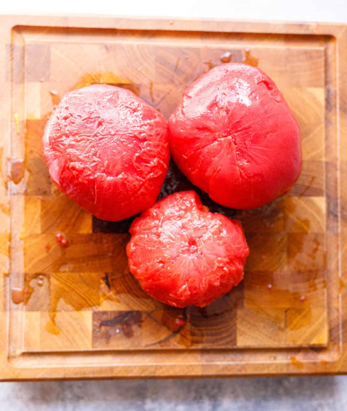 Three peeled tomatoes on a wooden cutting board after blanching