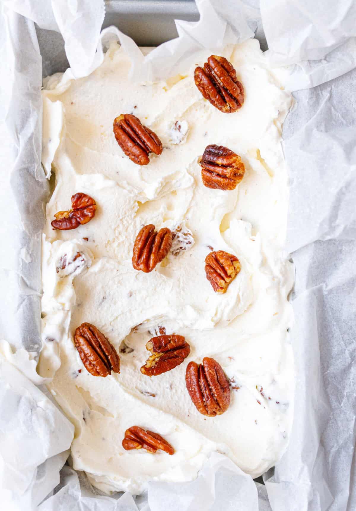 Homemade butter pecan ice cream in a loaf pan topped with buttery toasted pecans before freezing.