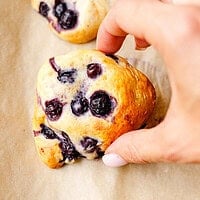 Hand picking up a baked cottage cheese blueberry scone from the tray