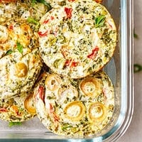 tack of baked egg white breakfast cups with spinach, roasted red pepper, green olives and feta in a glass meal prep container