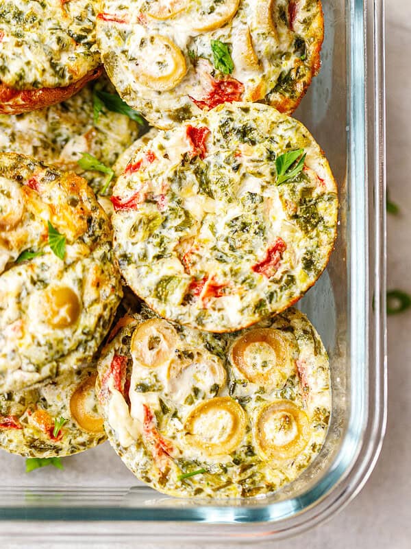 tack of baked egg white breakfast cups with spinach, roasted red pepper, green olives and feta in a glass meal prep container