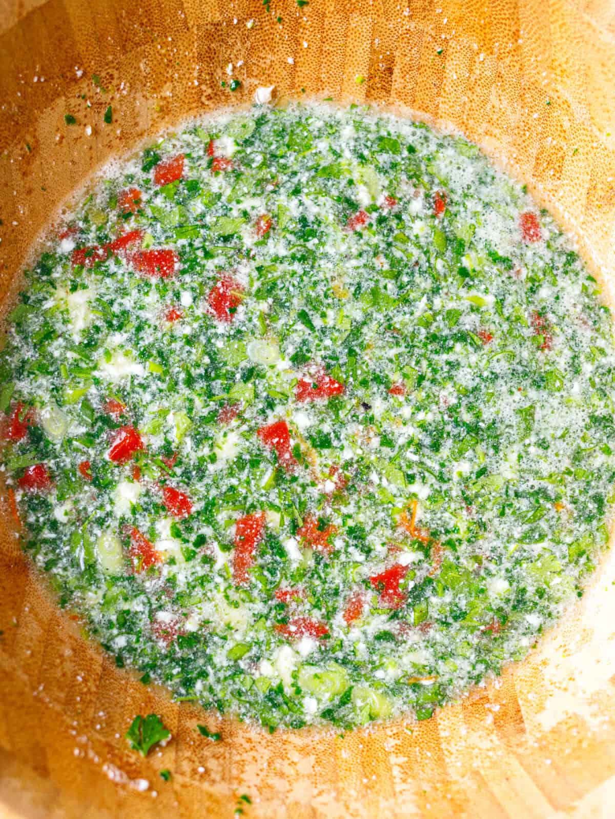 Egg white mixture in a wooden bowl with chopped spinach, roasted red pepper, green onion, parsley and crumbled feta