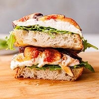 Side view of stacked fig and burrata toasts on a wooden cutting board