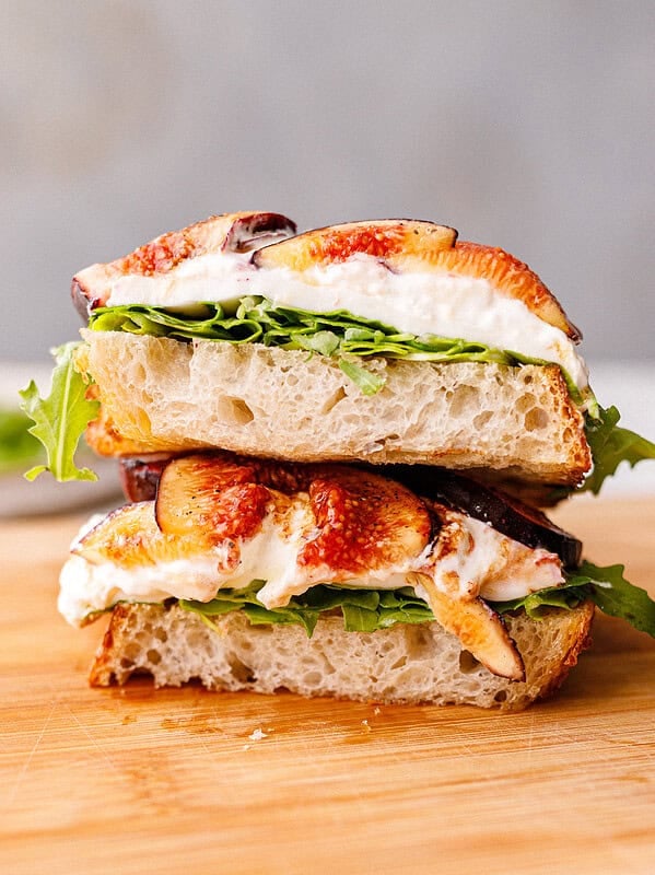 Side view of stacked fig and burrata toasts on a wooden cutting board