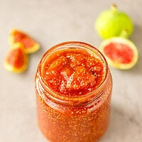 Glass jar of chunky fig jam full of tiny seeds, with halved green figs in the background