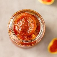 Overhead view of a whole peeled fig in glossy syrup inside an open glass jar