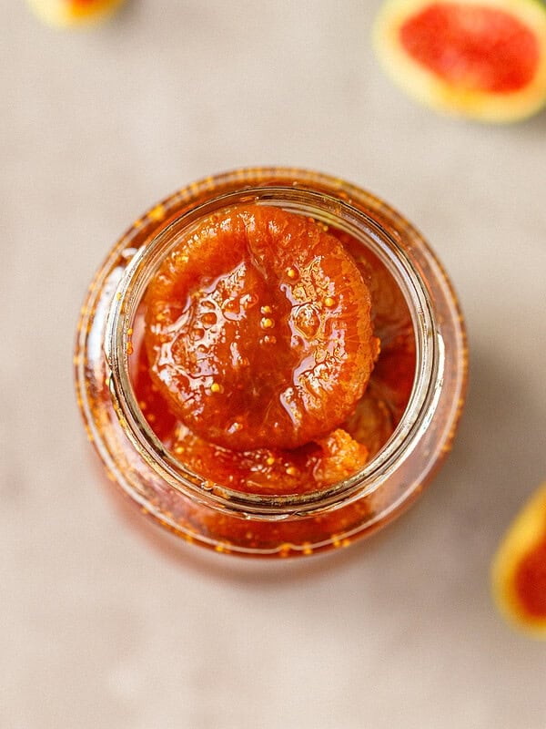 Overhead view of a whole peeled fig in glossy syrup inside an open glass jar