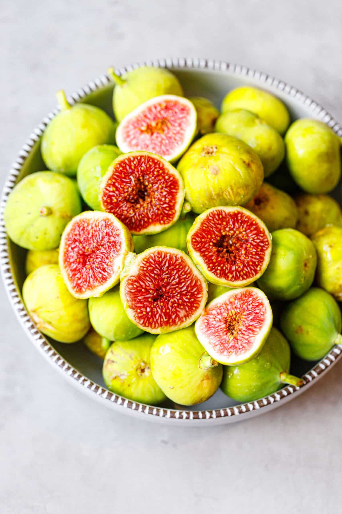Bowl of fresh green figs with several cut in half showing bright red centers