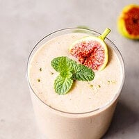Glass of pale pink fig smoothie with a green fig wedge and mint on a gray concrete surface