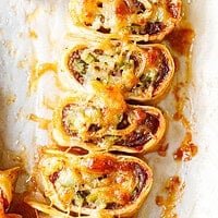 Baked ground beef tortilla pinwheels on parchment paper, cut side up, with melted browned cheese on top and a spiral of beef, chopped pickles and cheese inside.