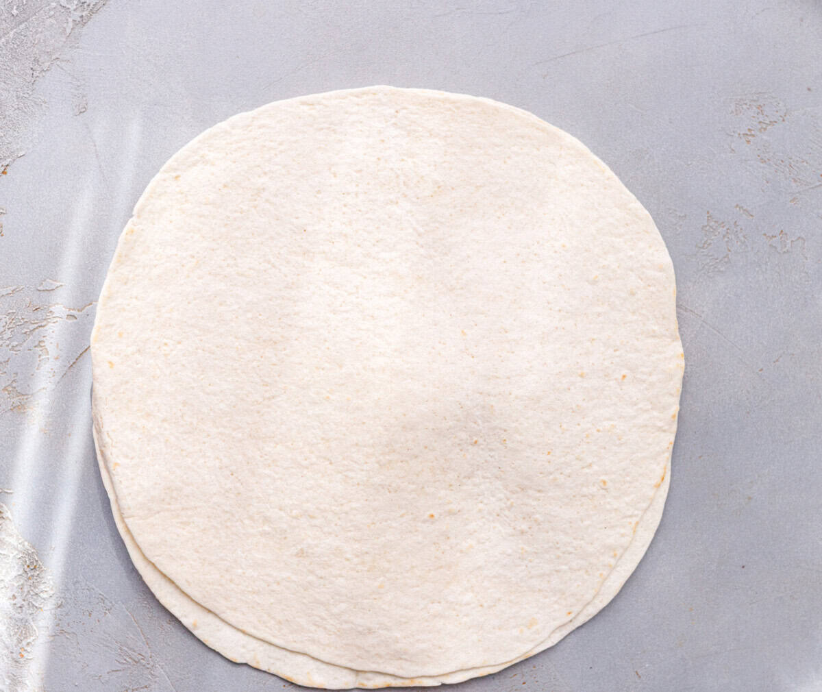 Two plain flour tortillas stacked on a grey surface.
