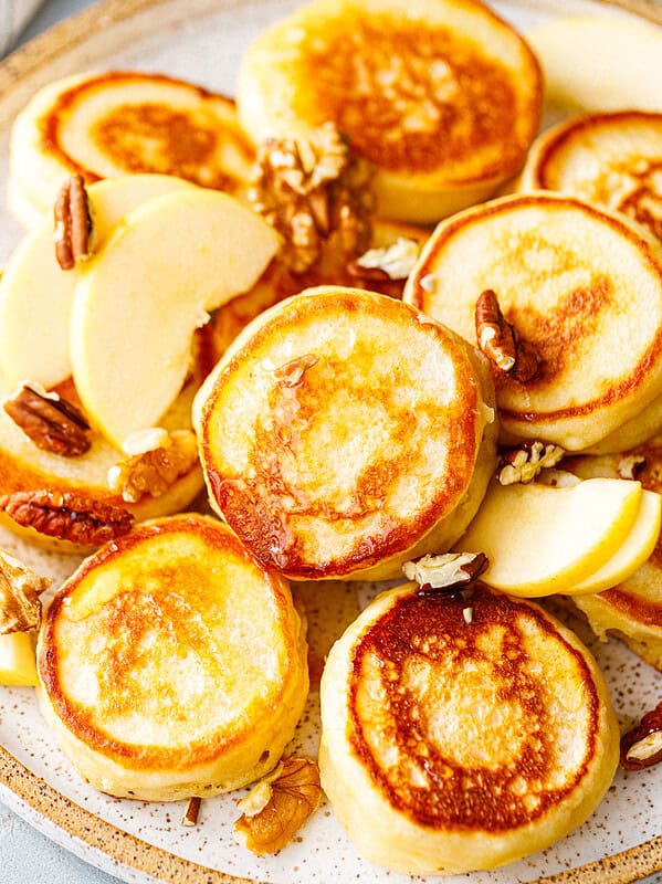 Close-up of golden kefir pancakes drizzled with honey and topped with walnuts and apple