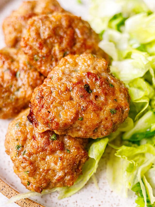 Juicy baked beef meatballs on a speckled plate with shredded iceberg lettuce salad