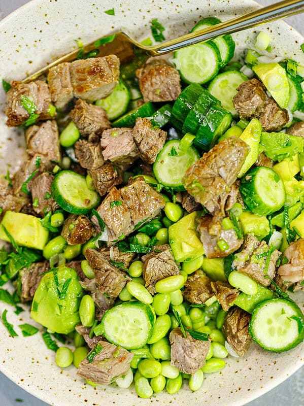 Steak avocado salad with edamame, cucumber, and herbs tossed in a bowl