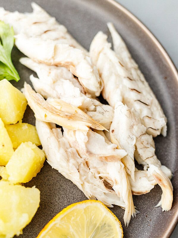 Flaked whole roasted branzino fillet next to potato salad, lemon slice and parsley