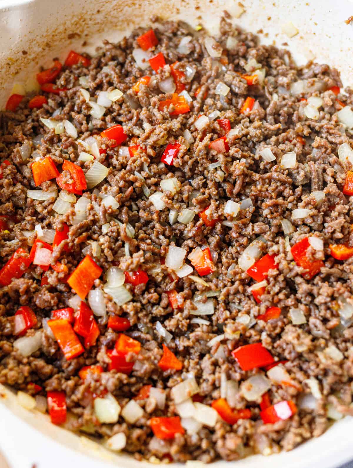 Browned ground beef sautéed with diced onion, red bell pepper and garlic in a white skillet.